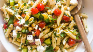 Cold pasta salad with italian dressing in white bowl and wooden spoon