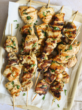 close up grilled chicken skewers on a white platter.