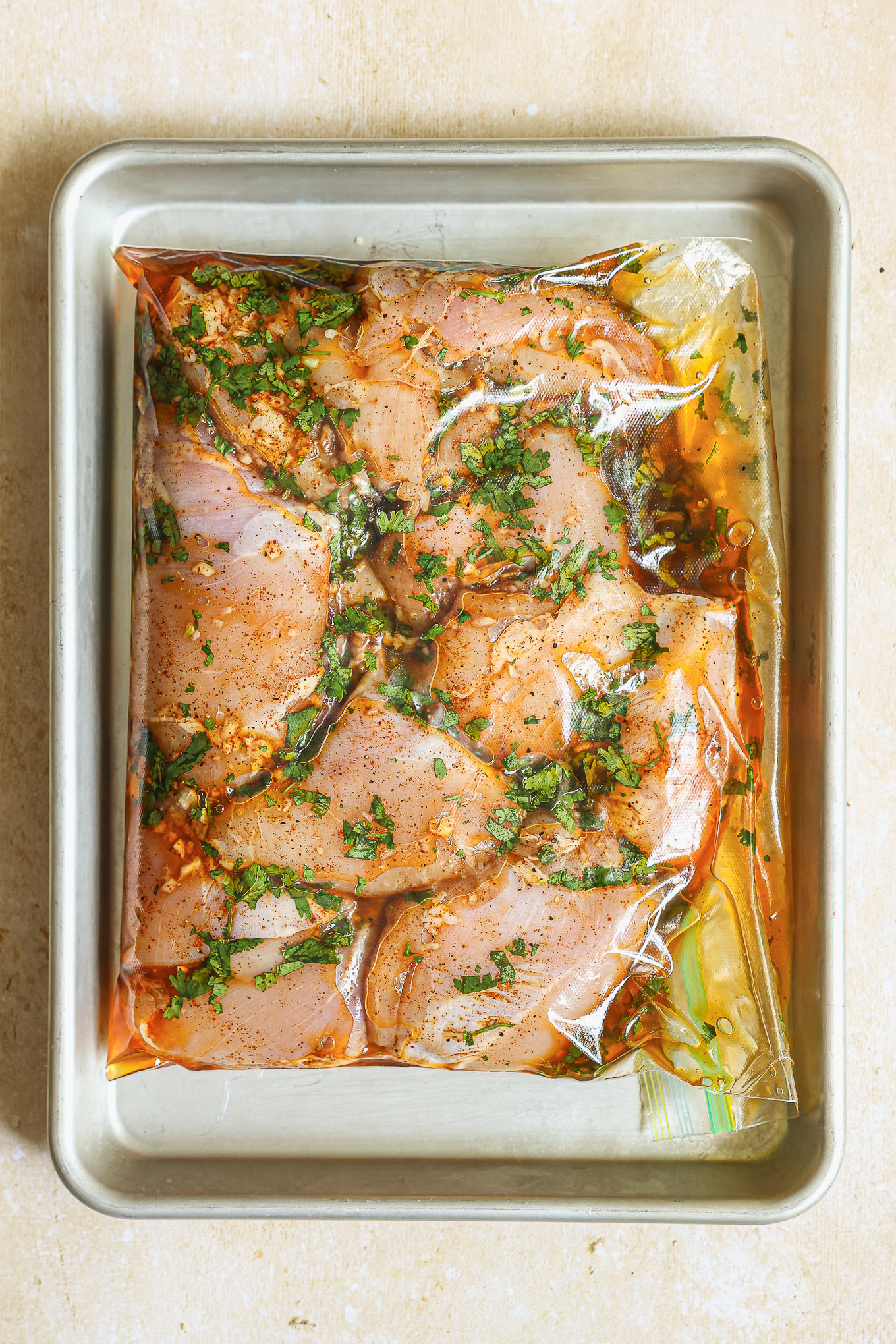 chicken inside ziploc bag laying on a baking sheet.