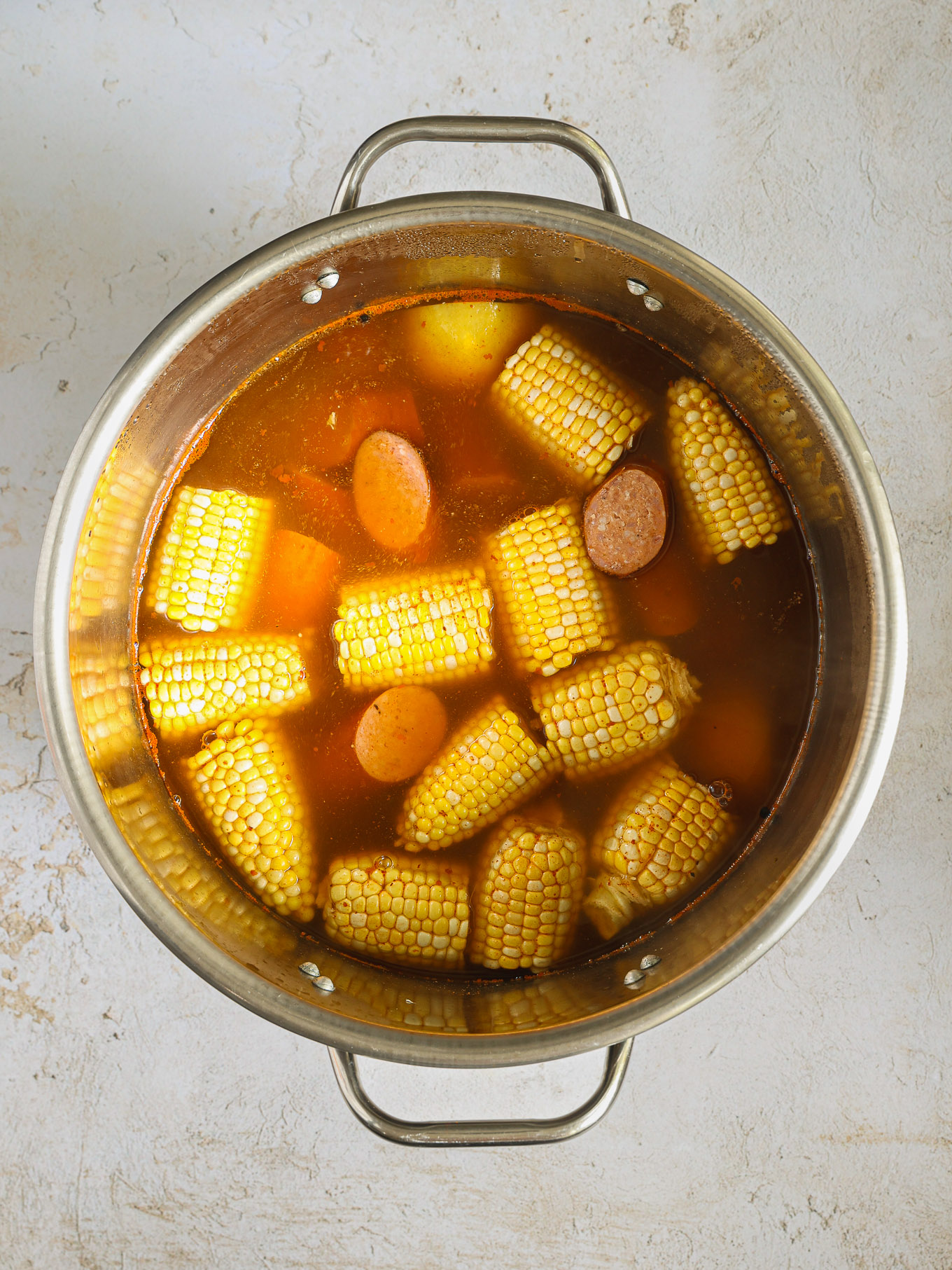 corn and sausages in broth in a pot.