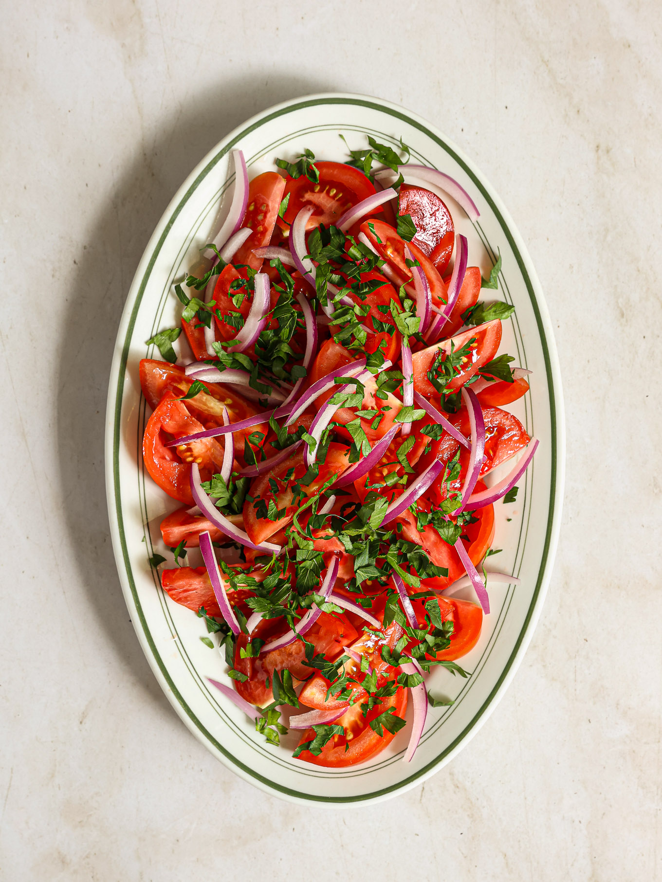 arranged tomatoes with red onions and parsley on oval platter.