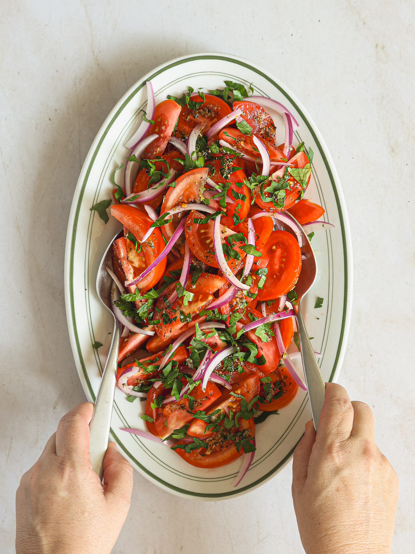 tomato salad being tossed with two spoons.