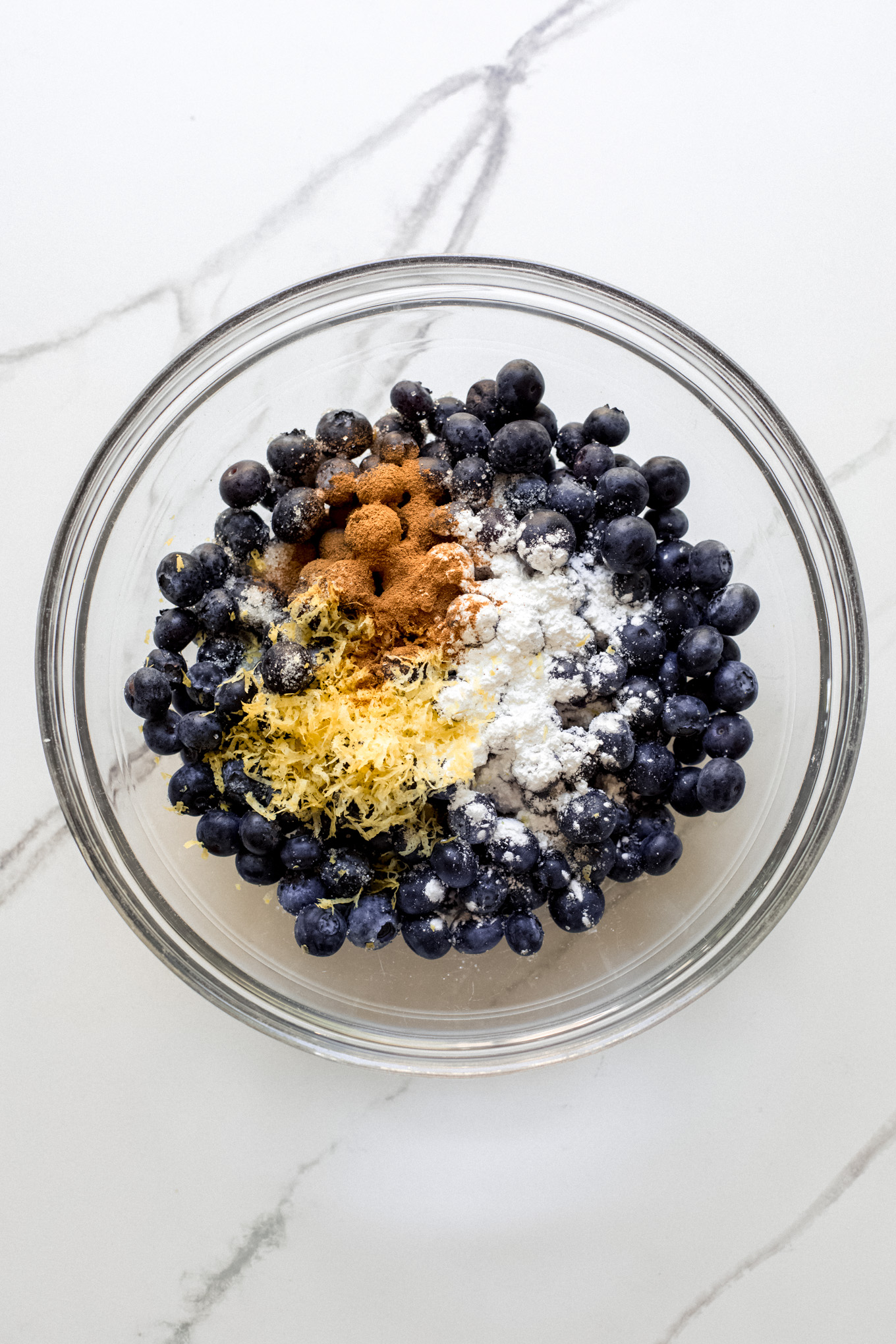 blueberries with lemon zest and cinnamon in a glass mixing bowl.